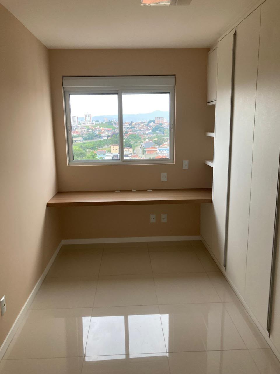 Home office com paredes em tom bege quente e acabamento liso ao redor da janela